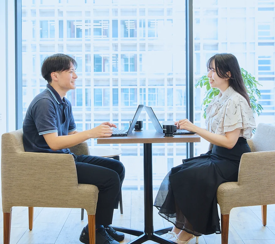 オープンスペースで若手社員が協力して業務を進める様子。部署や役職に関わらず意見交換が活発な社風。